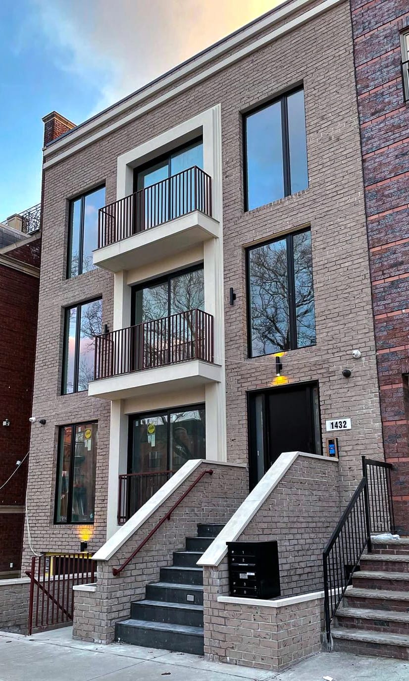 Brick residential facade with large windows, balconies, and a front stoop
