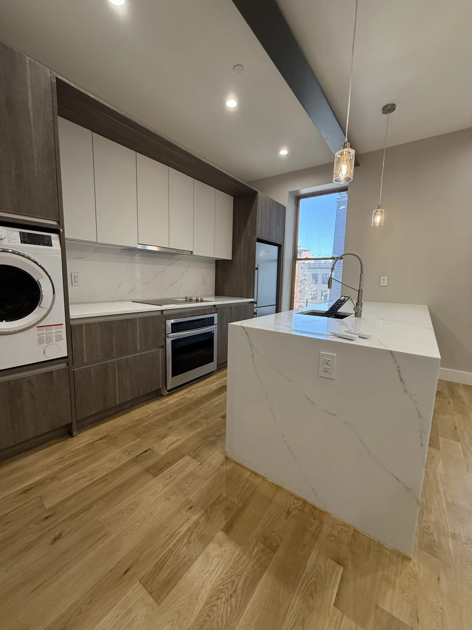 Apartment kitchen with two-tone cabinets, a light waterfall island, built-in appliances, and glass pendant lights