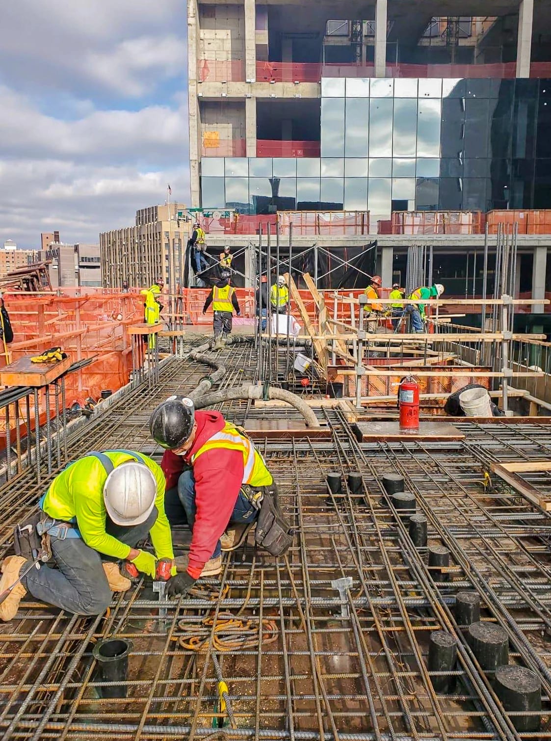 Workers tying reinforcing steel on a concrete deck beside a building under construction