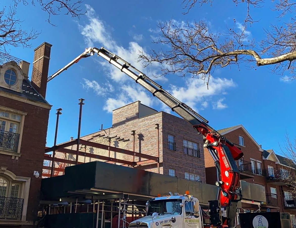 A crane lifting materials beside a brick building and steel framing