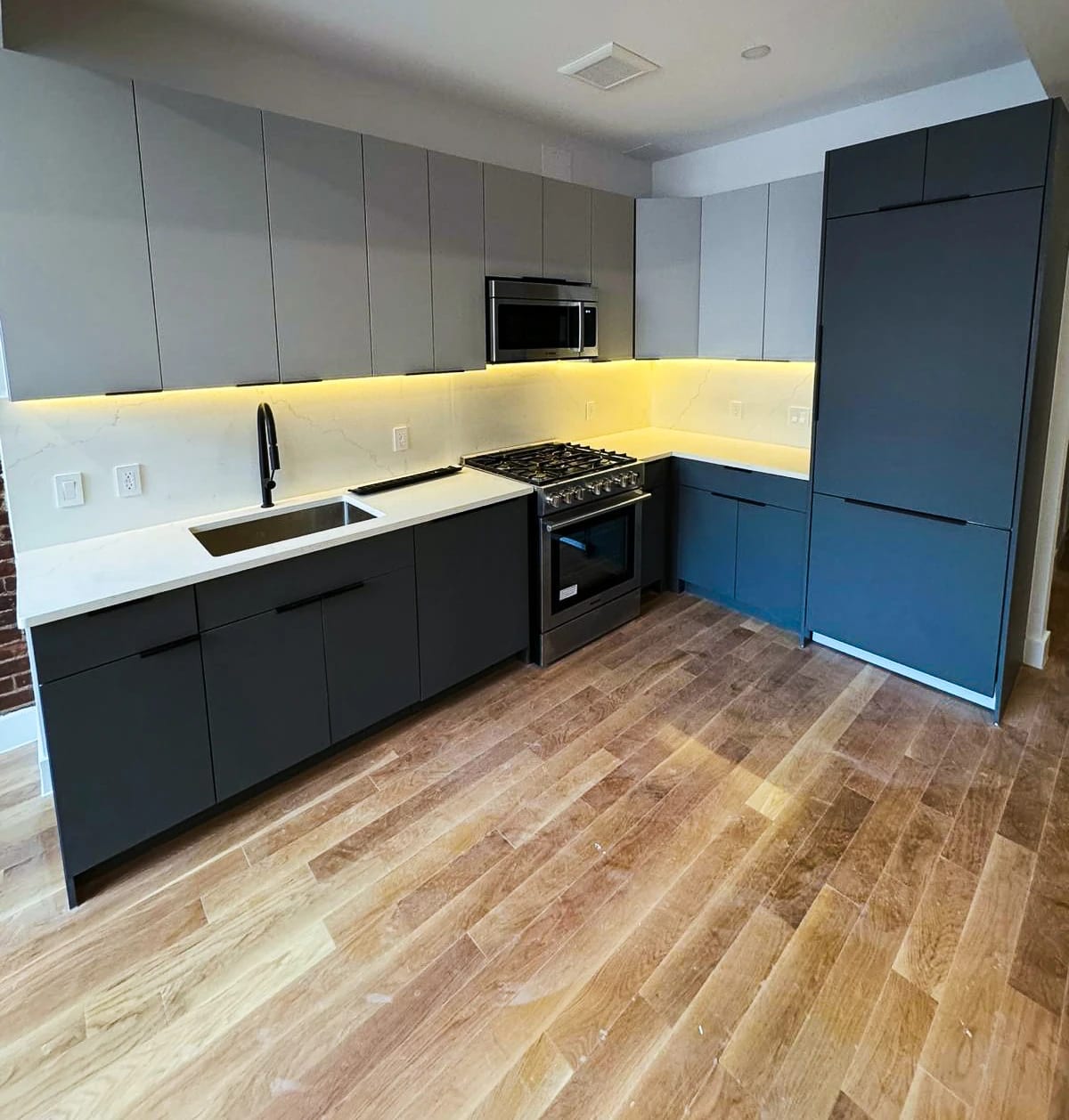 Kitchen with navy and gray cabinetry, white counters, and under-cabinet lighting