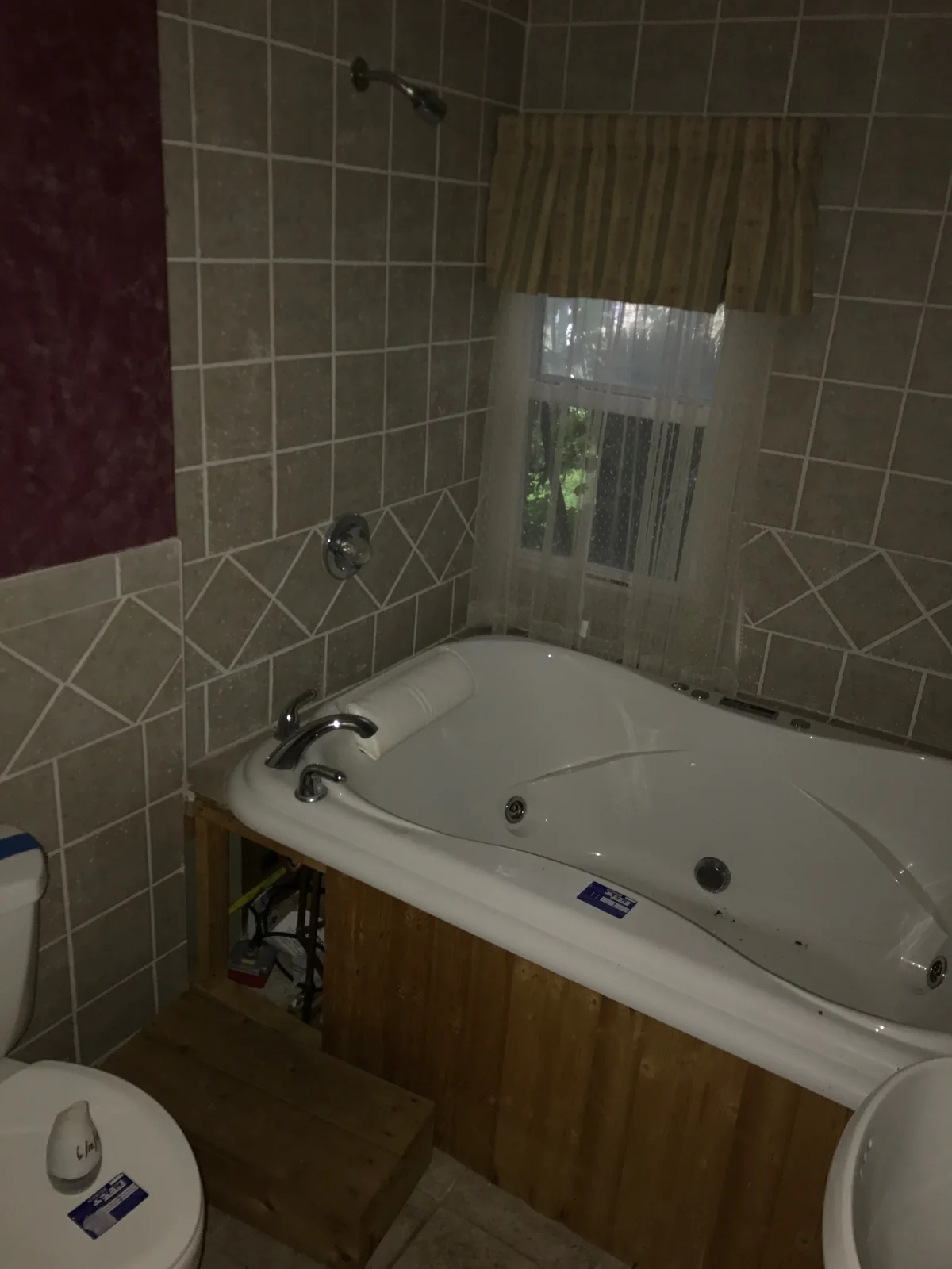 Bathroom before renovation with a jetted tub, tiled walls, and a window