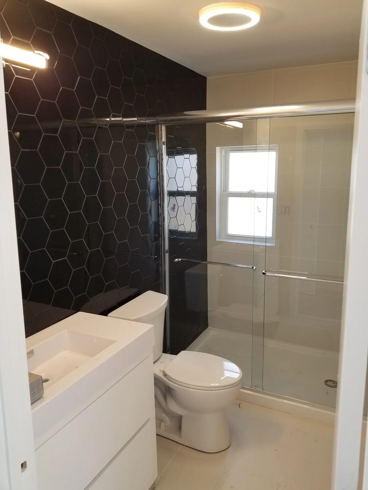 Bathroom with dark hexagonal wall tile, a white vanity, toilet, and glass shower enclosure