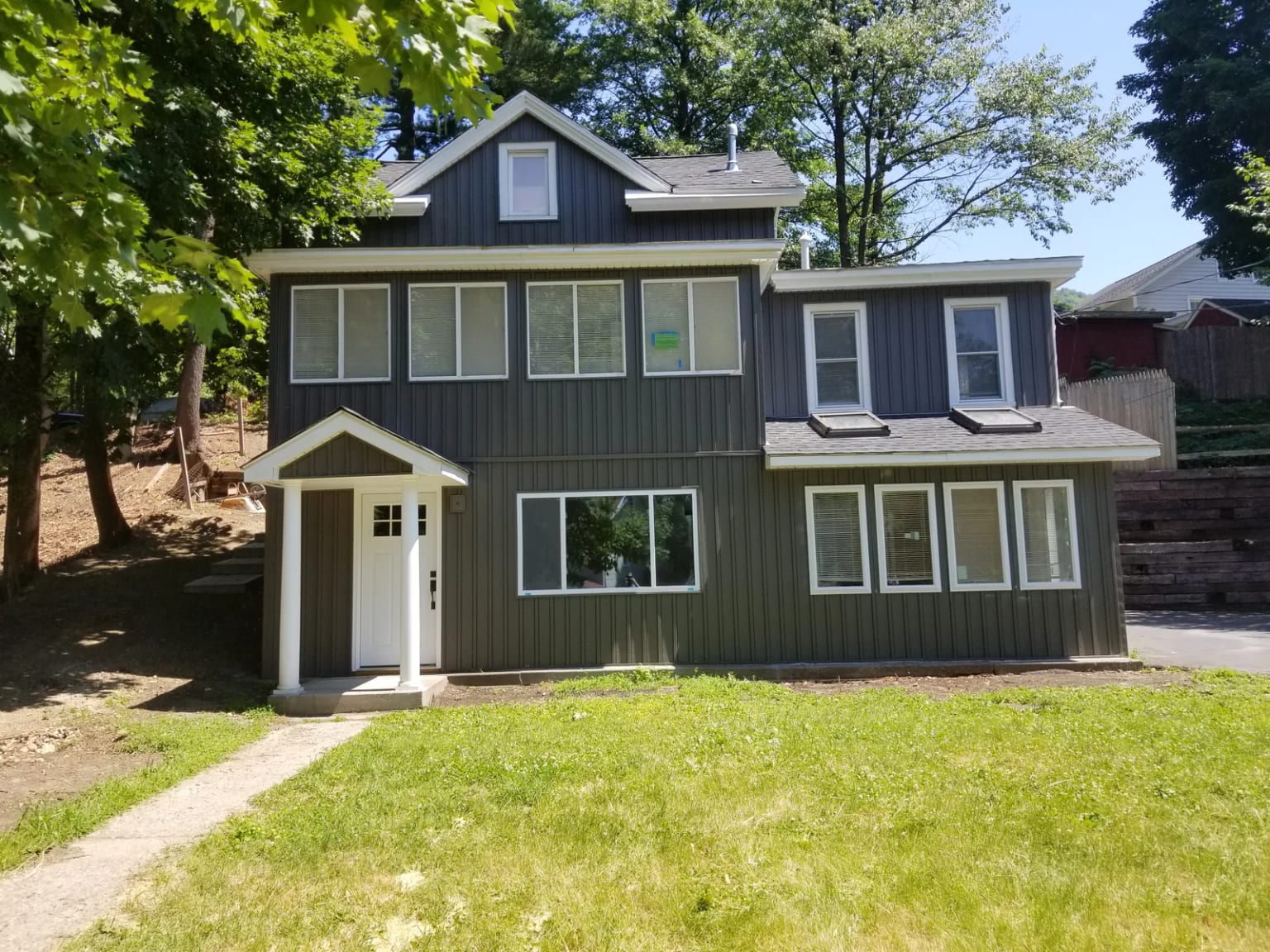 Front elevation with vertical siding, white trim, covered entry, and lawn