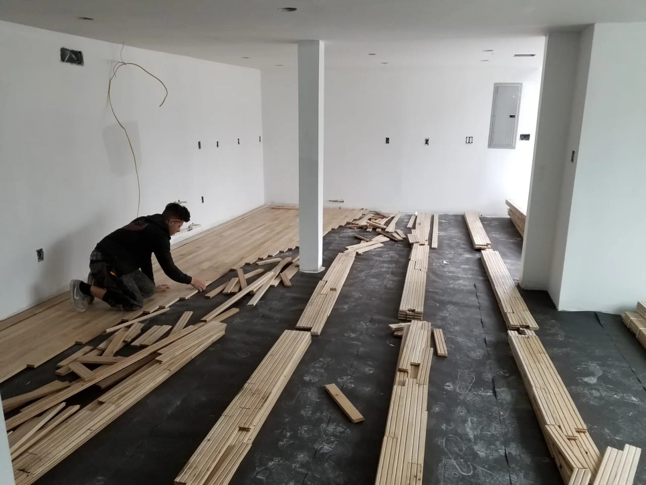 Worker installing wood flooring on the first floor beside stacked boards