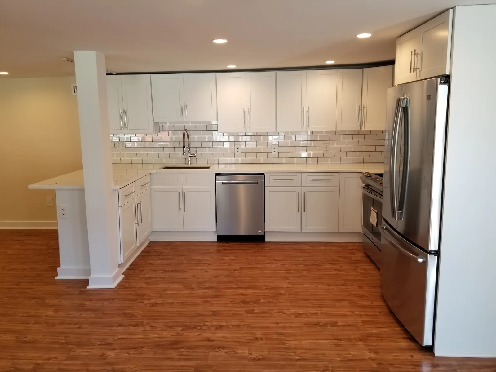 Renovated kitchen with white cabinetry, a tiled backsplash, stainless steel appliances, and wood flooring