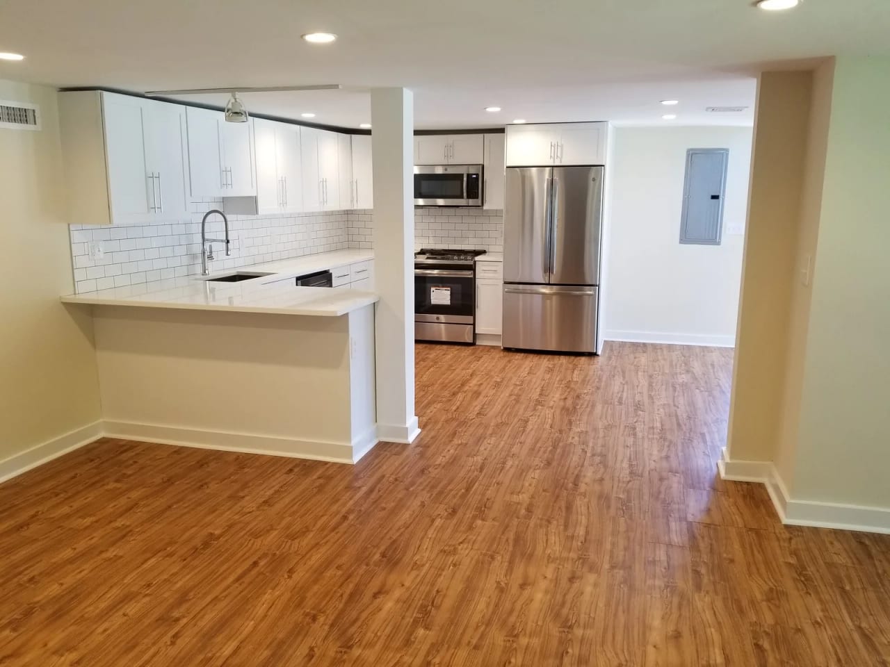 Wide view of the renovated kitchen with white cabinets, stainless steel appliances, and wood flooring