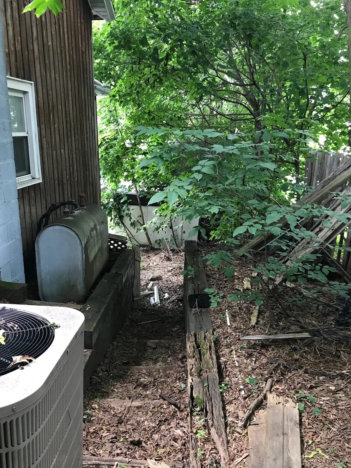 Old exterior tank beside the house, a condenser, and overgrown ground