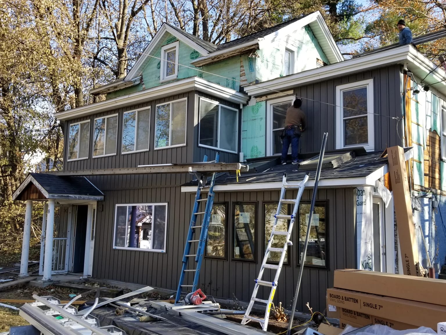 Workers installing vertical siding around the house windows with ladders in place