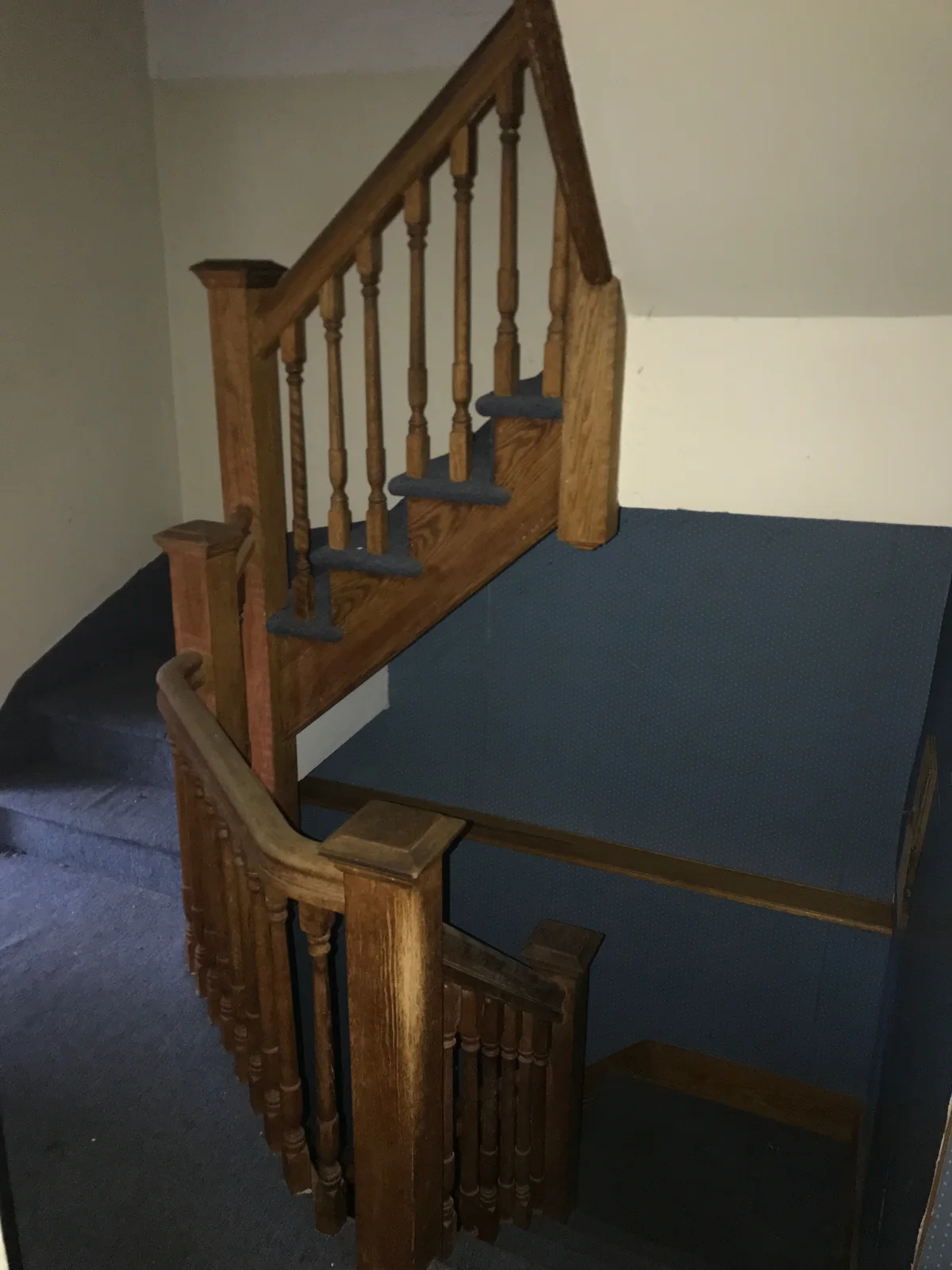 Existing wood staircase with turned balusters and blue carpeting before renovation