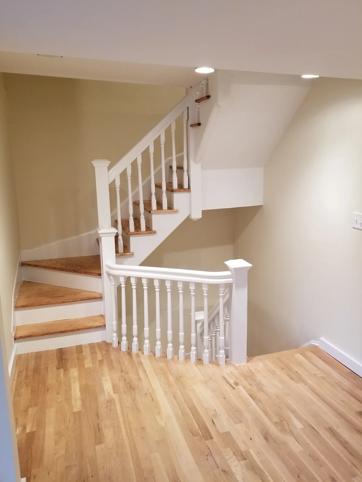 Refinished staircase with wood treads, white railings and risers, and wood flooring