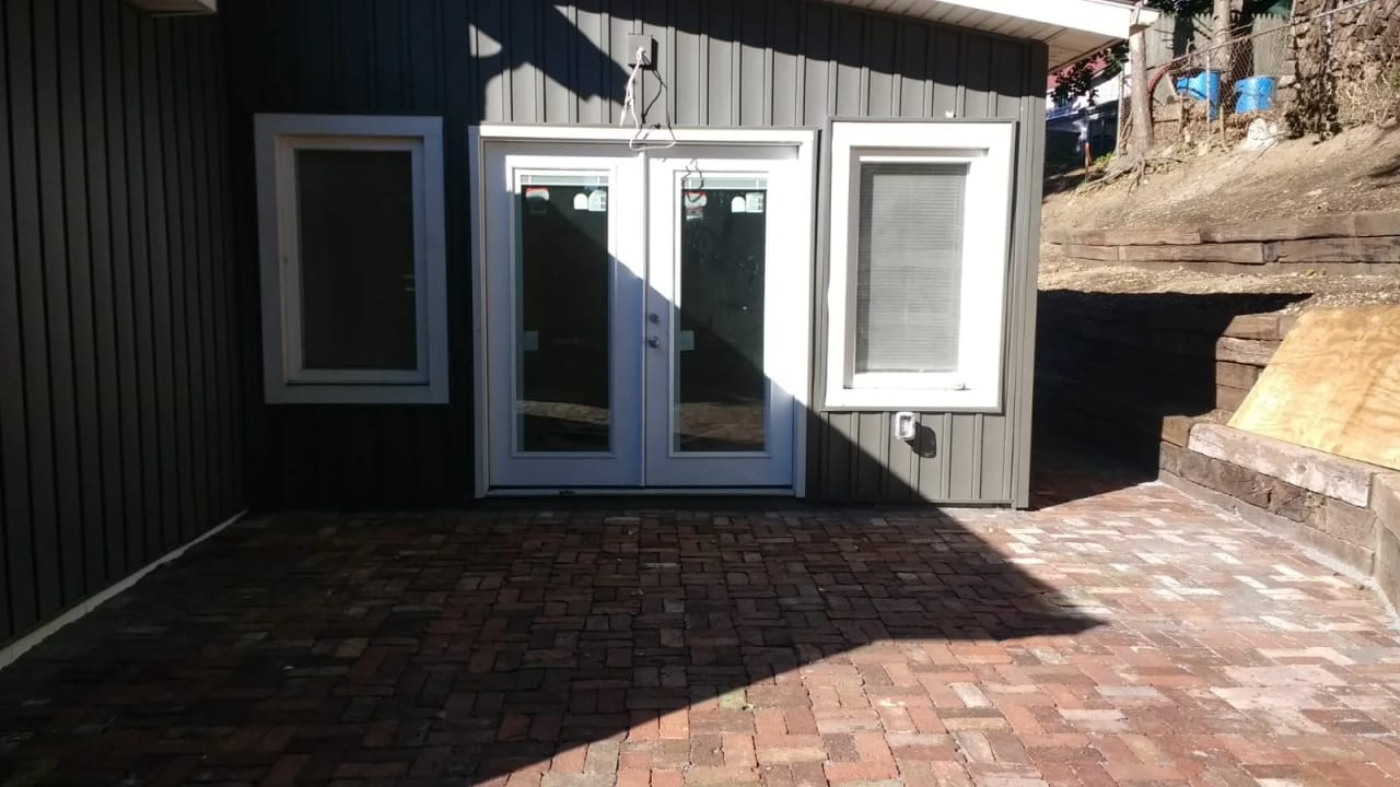 Glazed exterior doors beside a paved outdoor area, steps, and a retaining wall