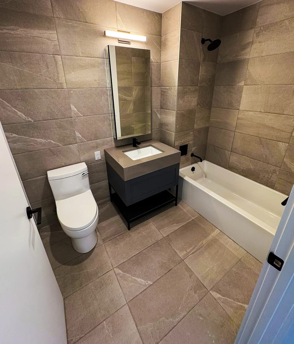 Bathroom with stone-colored tile, a gray vanity, and black fixtures