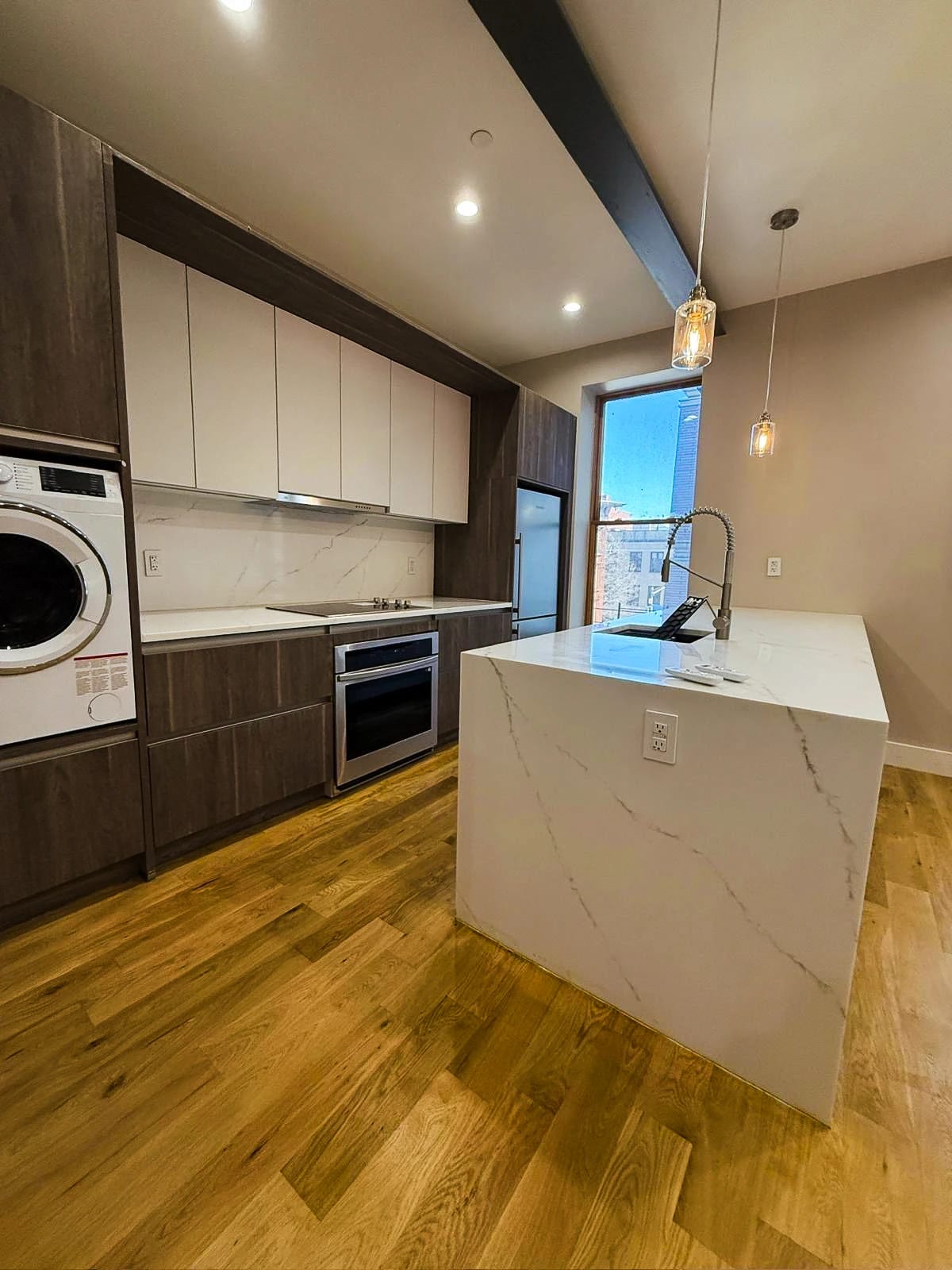 Kitchen with wood cabinetry, a white waterfall peninsula, and pendant lighting
