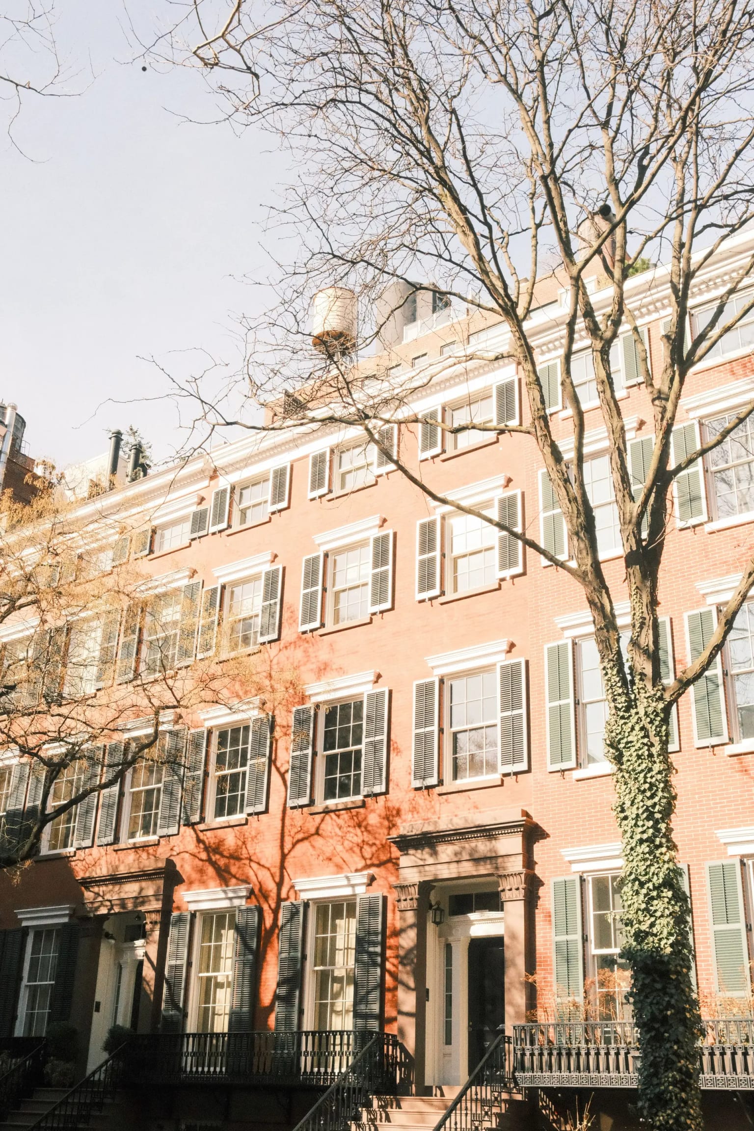 Row of brick New York townhouses with front stoops and green shutters