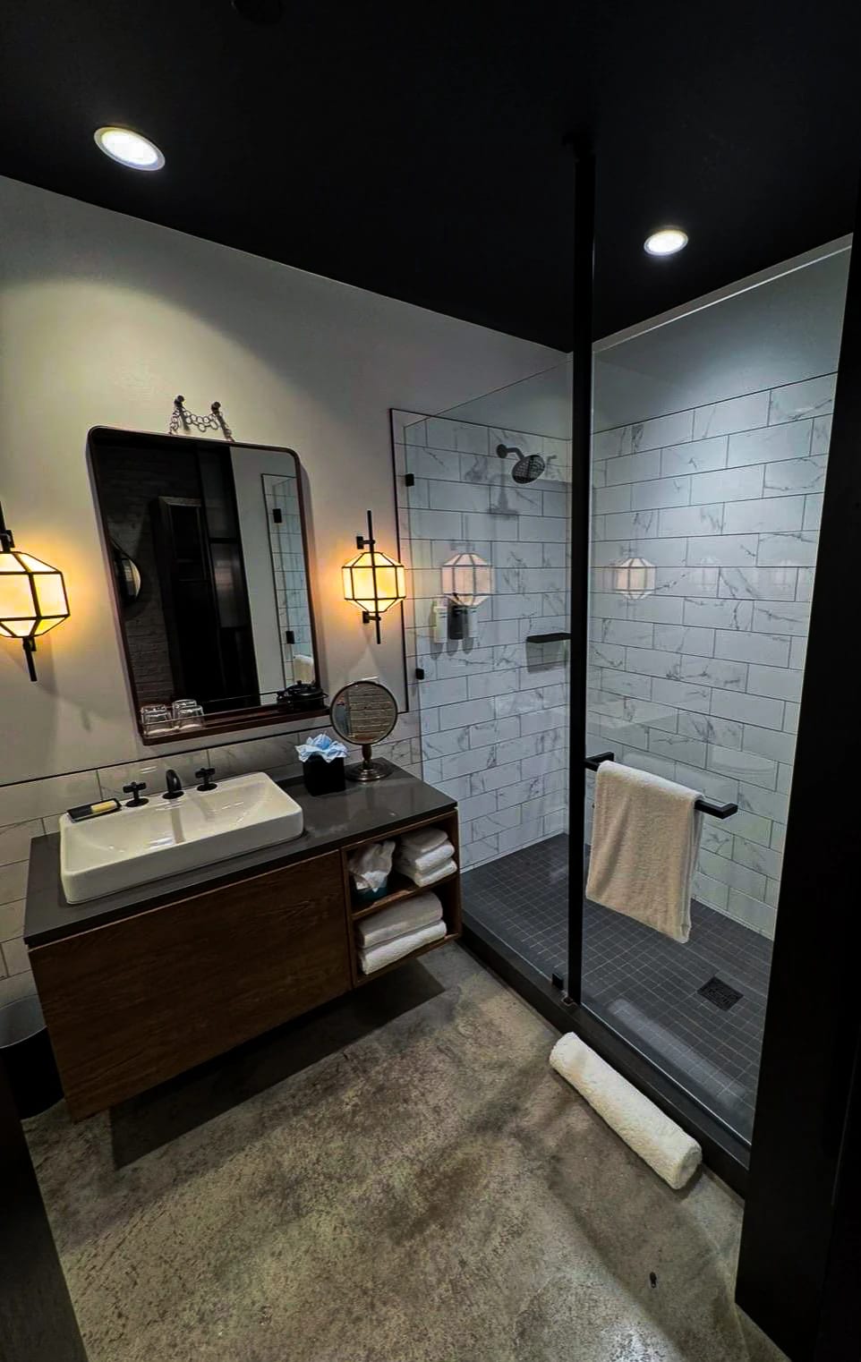 Glass shower enclosure beside a wood vanity beneath a dark ceiling