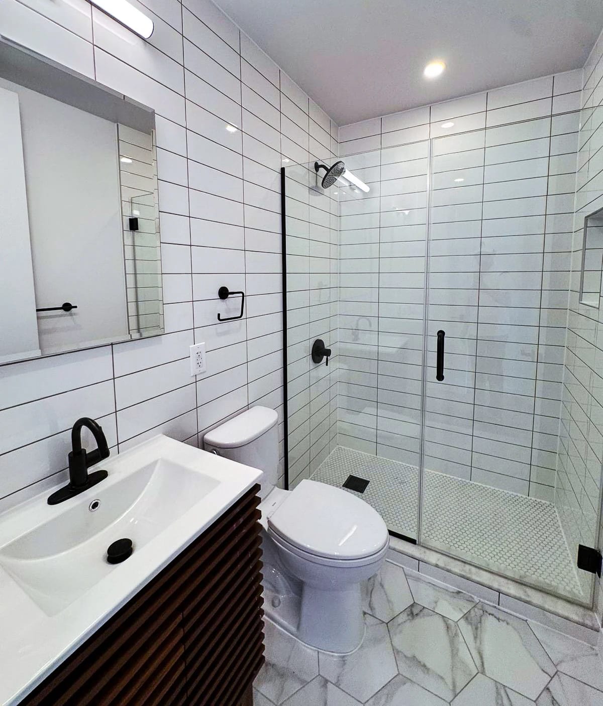 White tiled bathroom with black fixtures, a glass shower enclosure, and a wood vanity